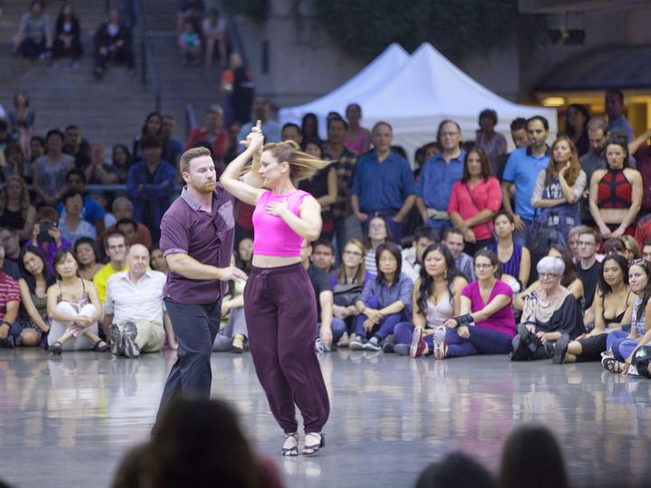 A salsa couple performs a demonstration in front of a seated crowd at an outdoor plaza