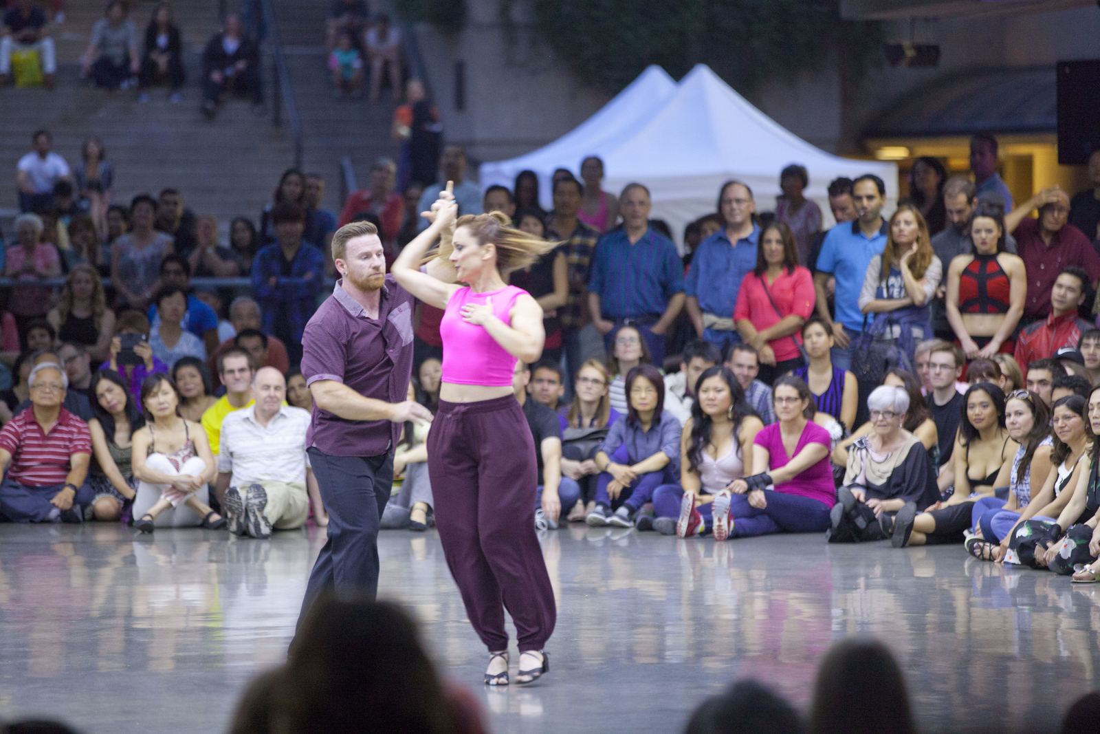 A salsa couple performs a demonstration in front of a seated crowd at an outdoor plaza