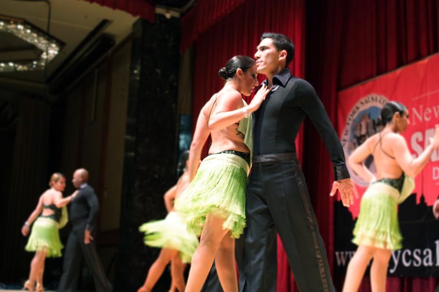 Salsa dancers in matching green outfits perform on a stage in New York