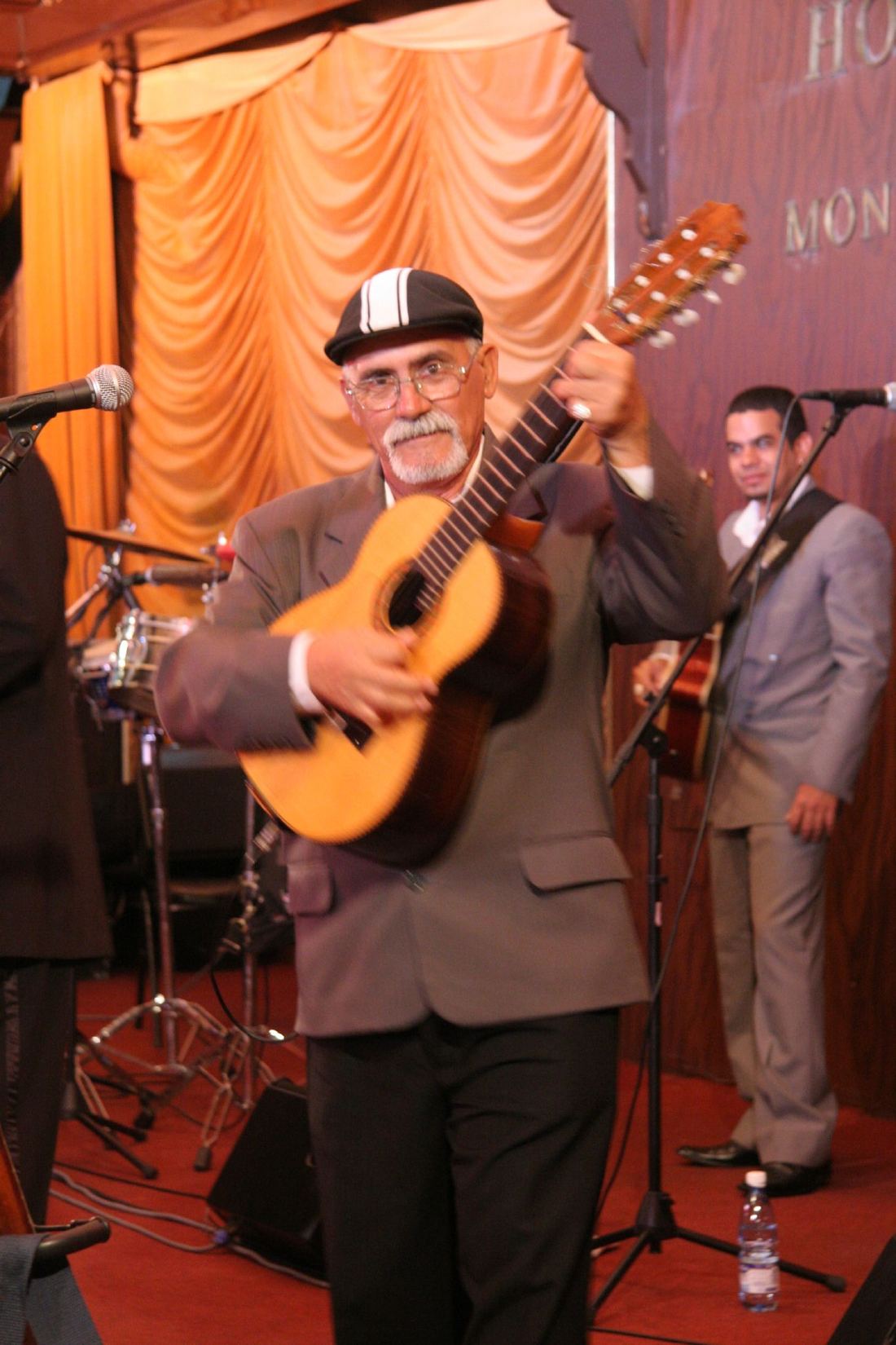 A singer with a small guitar performs with a Cuban band on stage